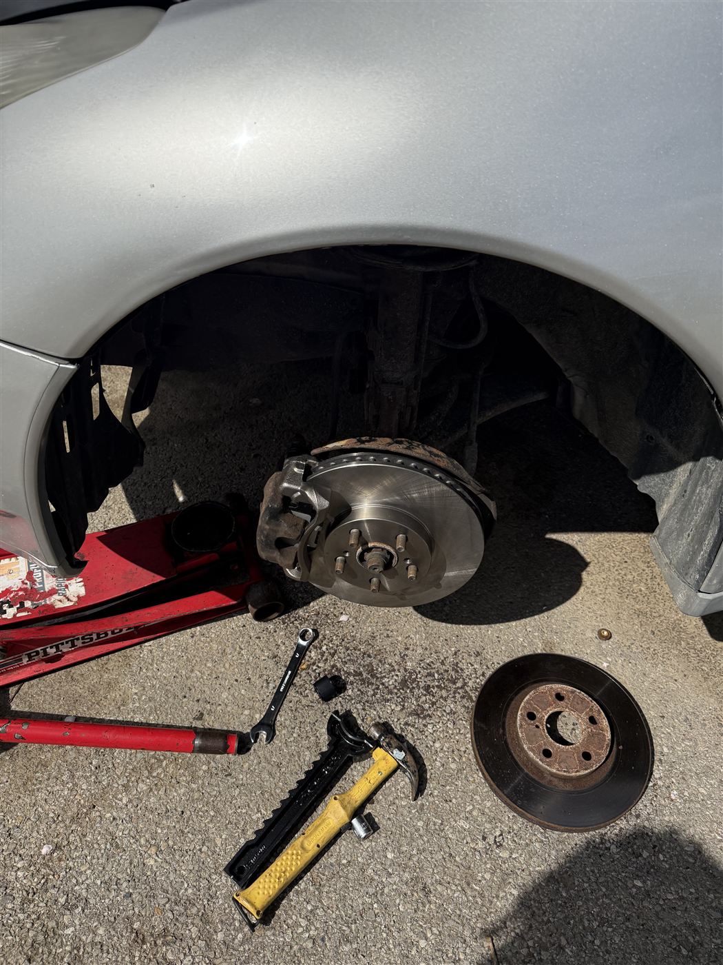 Front wheel removed with the old brake rotor set aside on the ground and tools laid out during a brake job
