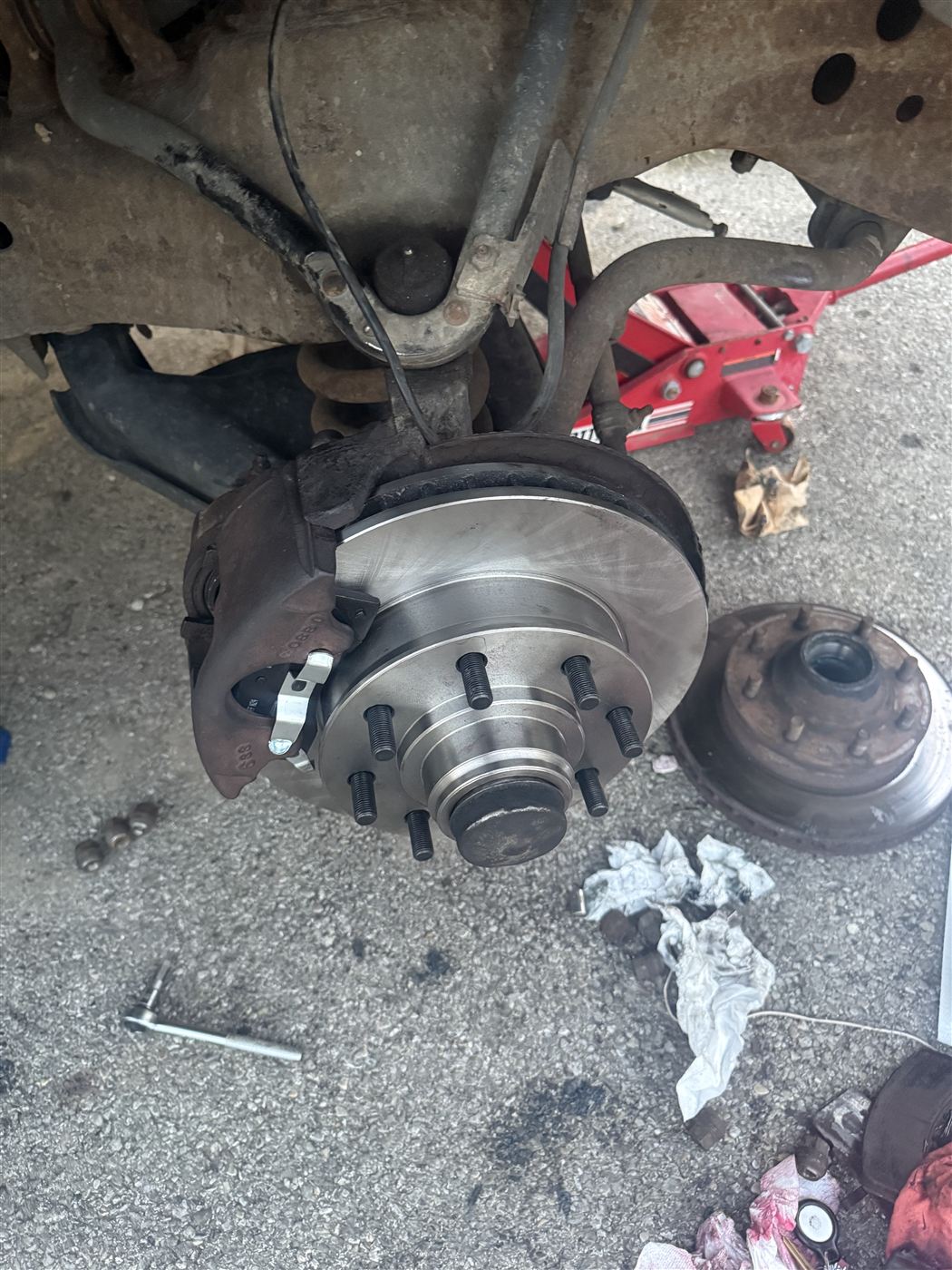 New rear brake rotor and caliper installed on the hub, with the old hardware set aside