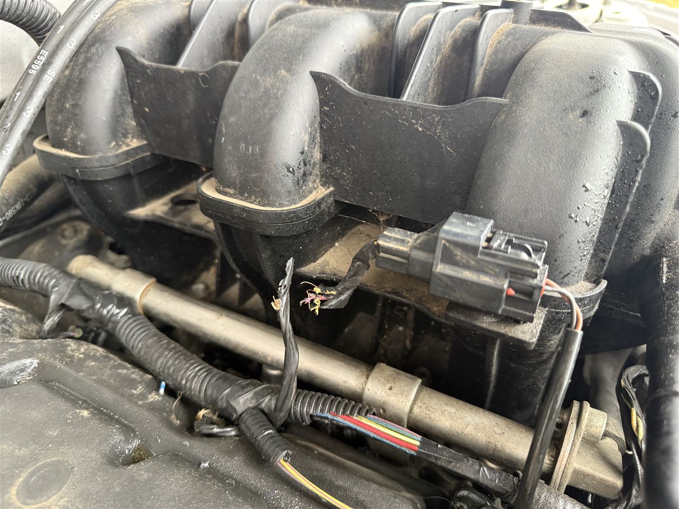 Damaged engine bay wiring harness under the intake manifold, exposed during an electrical diagnostic and repair